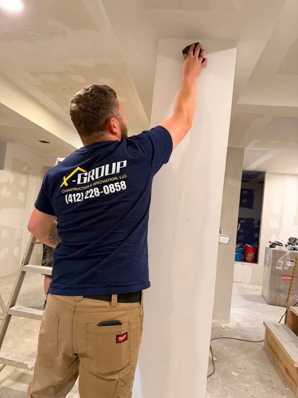 A man in construction attire smoothing drywall in an interior space under renovation.