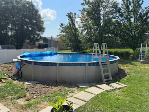 Above ground swimming pool on grass with ladder, cover, and garden in backyard.