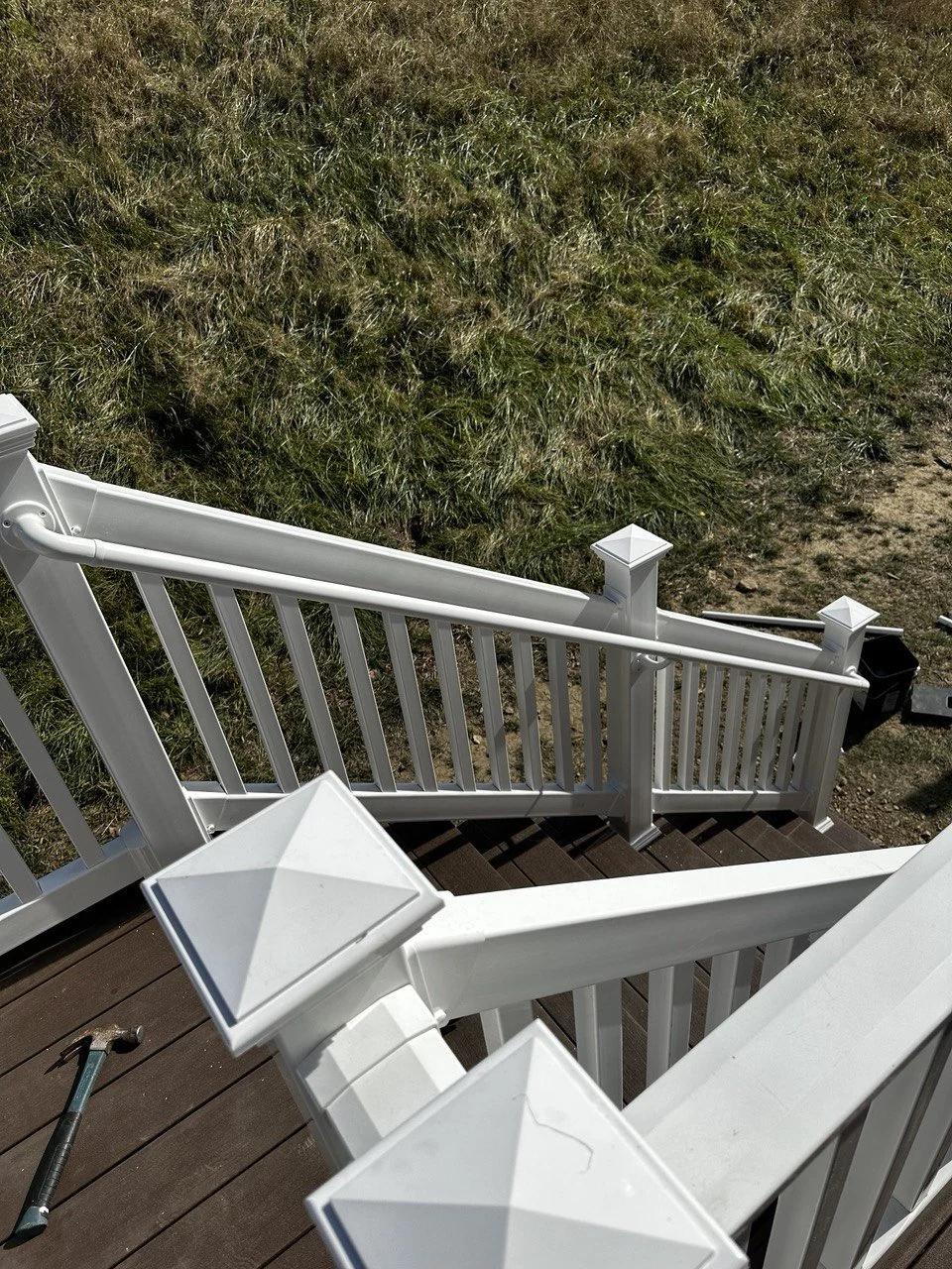 View of a white wooden staircase with decorative newel caps on a porch, overlooking grass and dirt ground outside.