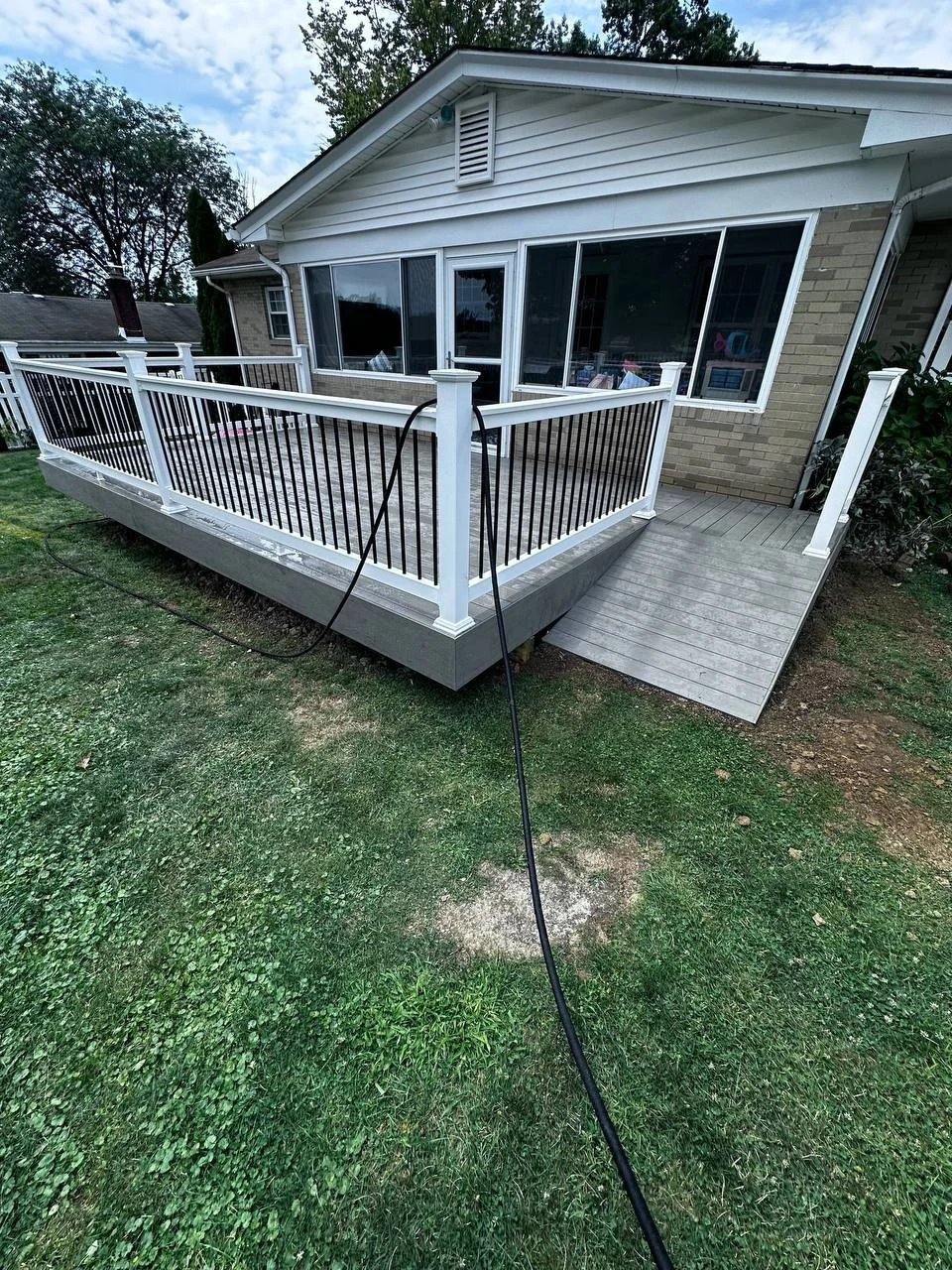 Backyard with wooden deck attached to a house, surrounded by a grassy yard, with trees in the background.