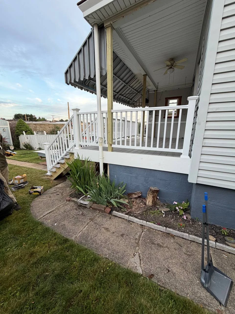 Back porch area with white railing, stairs, and an awning over the porch, with landscaping and tools nearby.