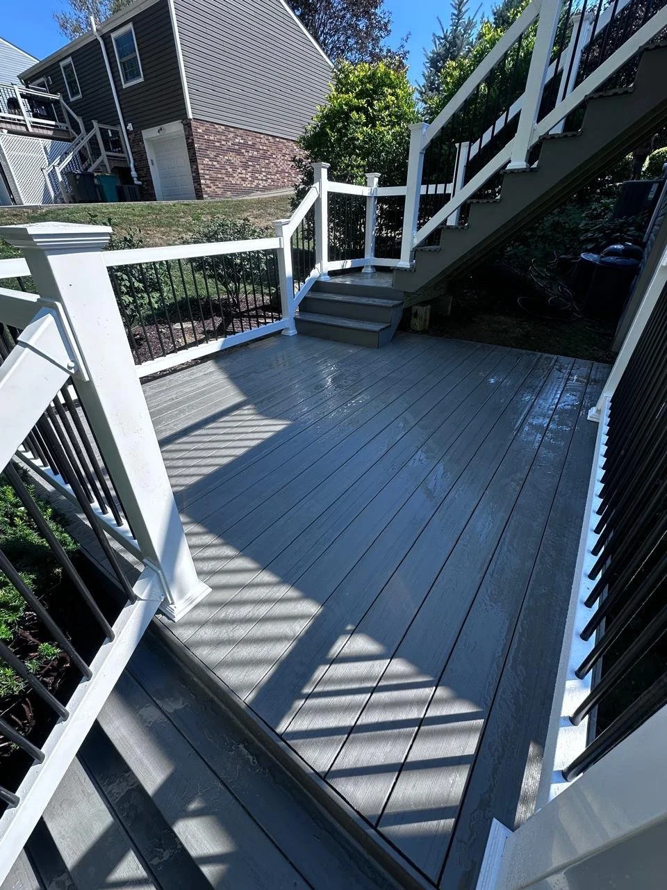 A clean, recently painted wooden deck with black and white railings, stairs leading to a backyard, and neighboring houses visible in the background on a sunny day.