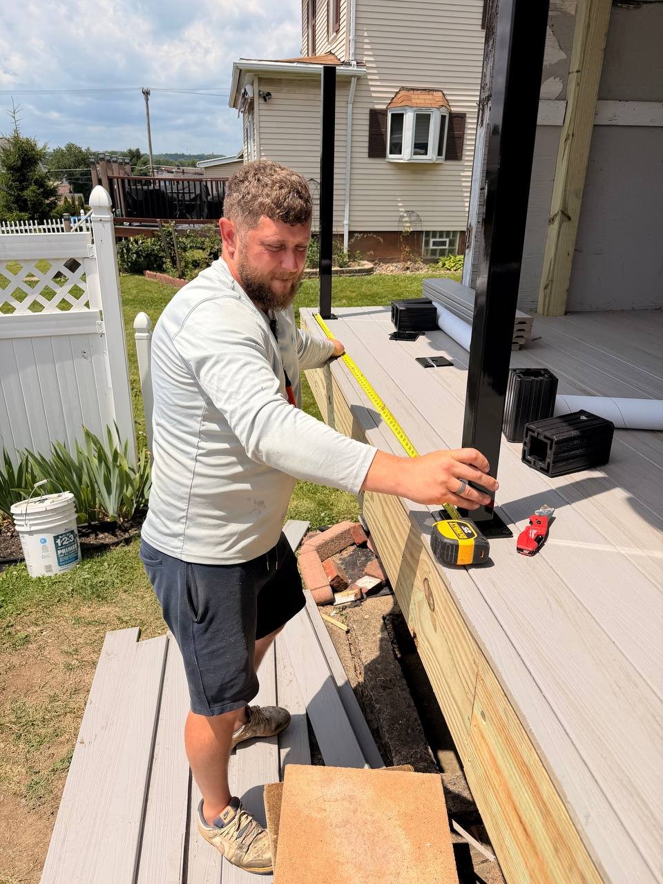 Man working on a construction project, measuring and assembling parts on a deck during daytime.