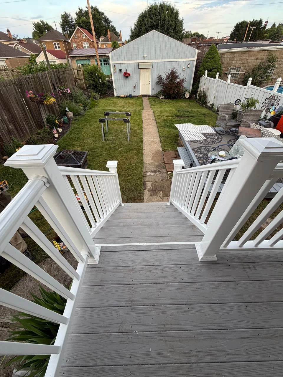 View from a deck stairs looking down onto a backyard with a lawn, garden, shed, and outdoor furniture.