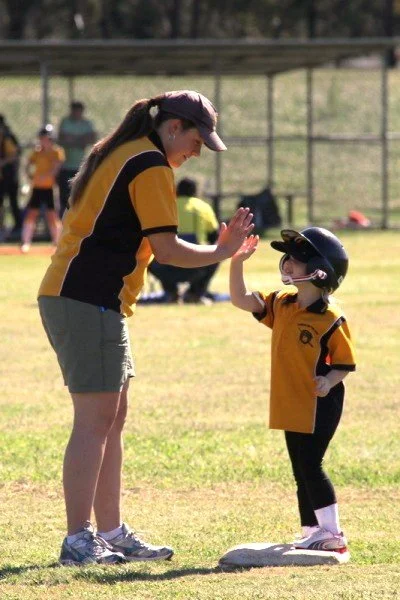 A young girl and a woman, likely a coach or parent, giving each other a high five on a baseball field.