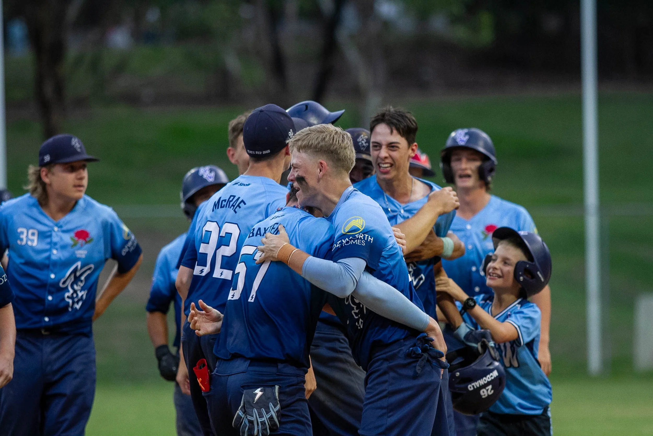 Baseball players in blue uniforms celebrating on the field, with some wearing helmets and others wearing gloves, during daylight.