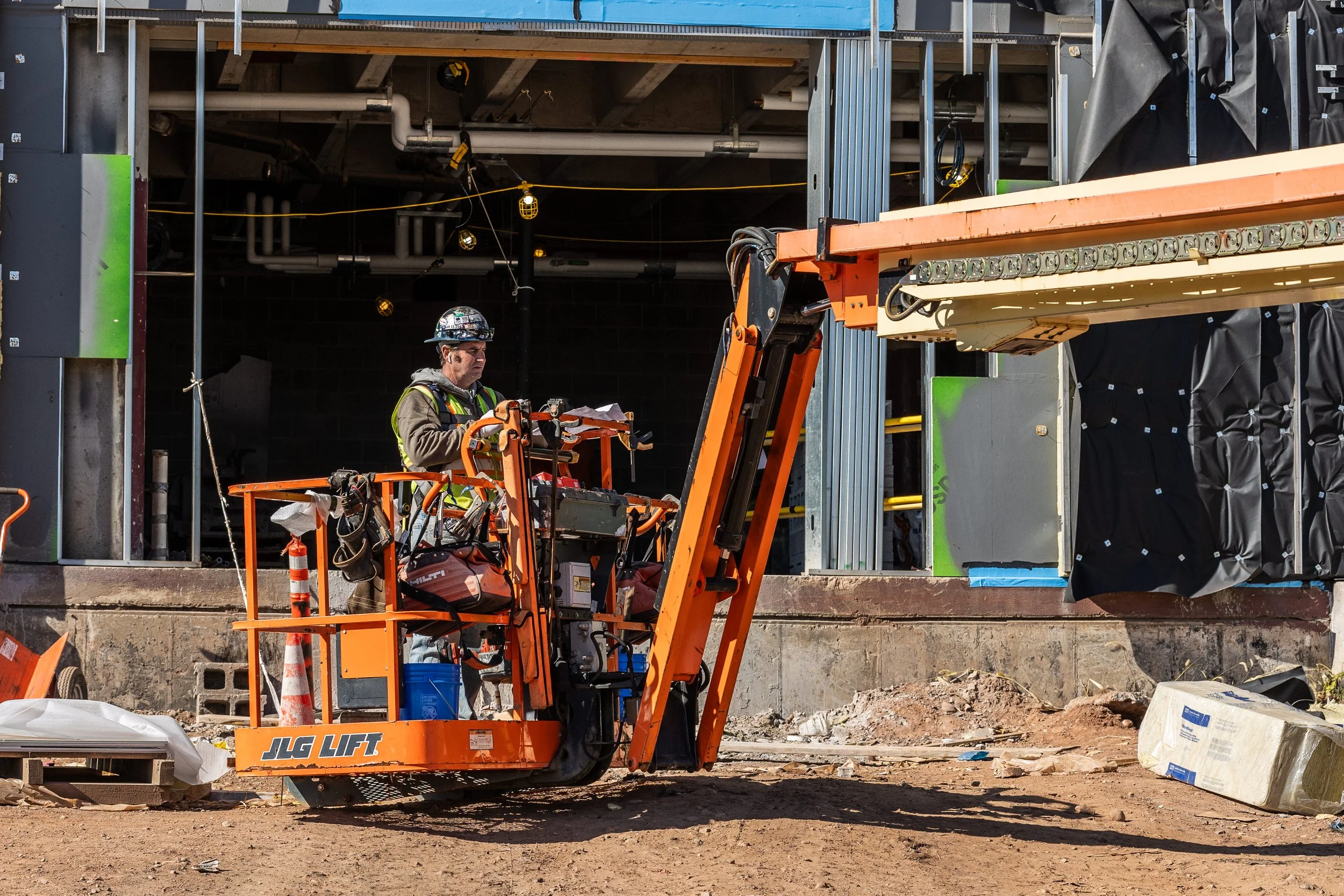 A construction worker operating an orange JLG lift at a building site.