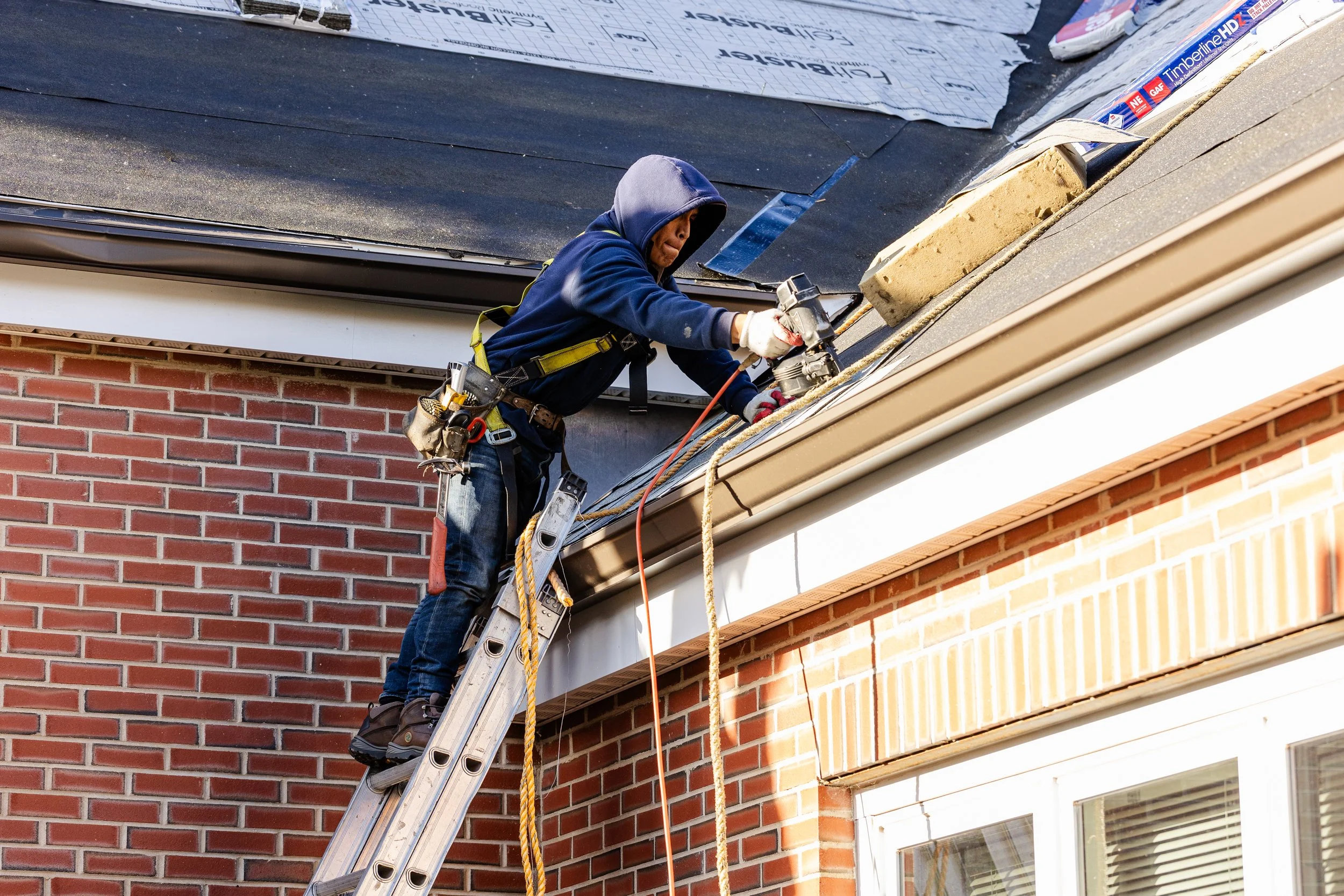 A worker on a ladder repairing a roof on a brick house.