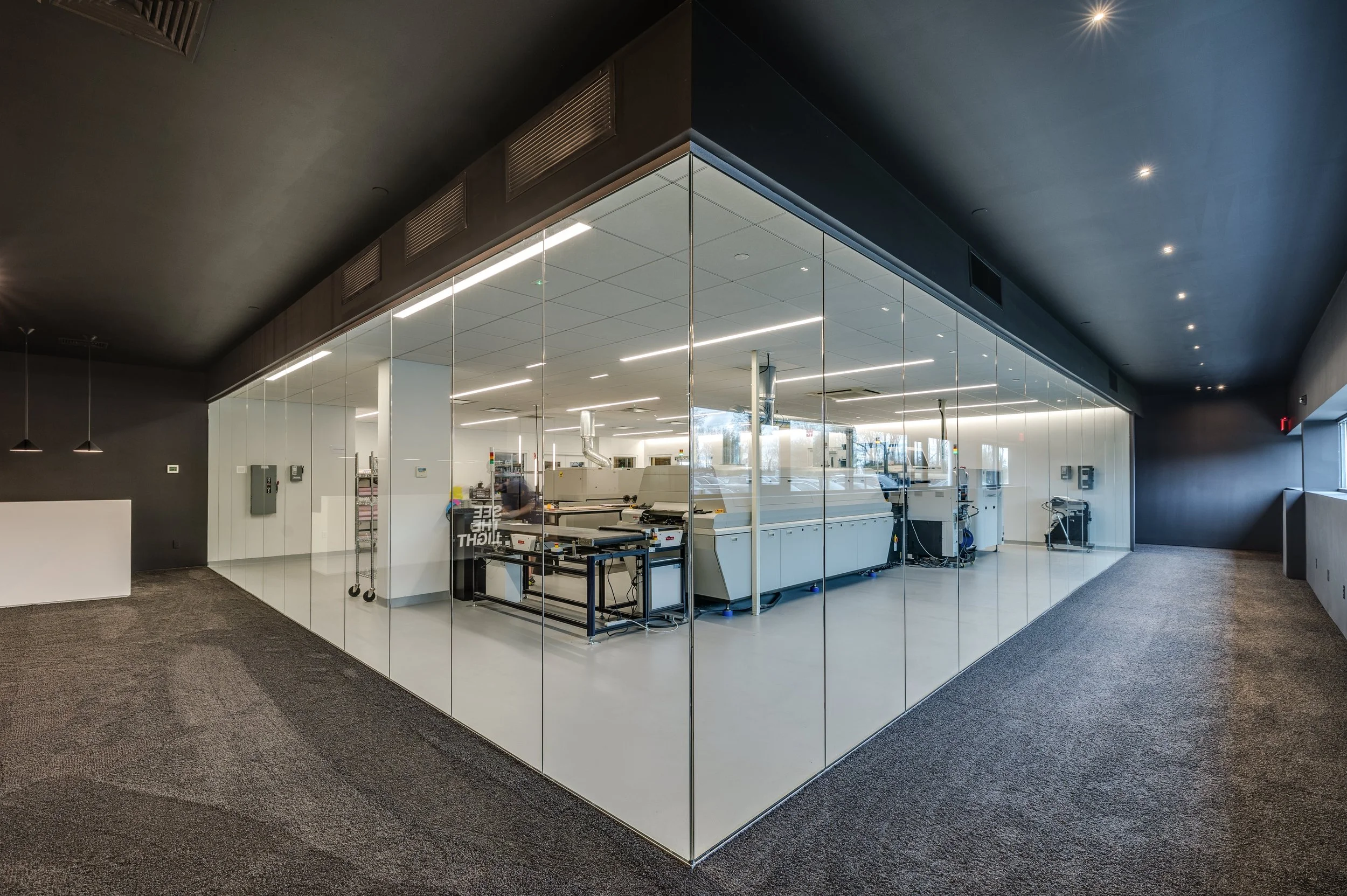 View of a modern office or conference room with glass walls, showing a space with machines and equipment inside, illuminated by ceiling lights.