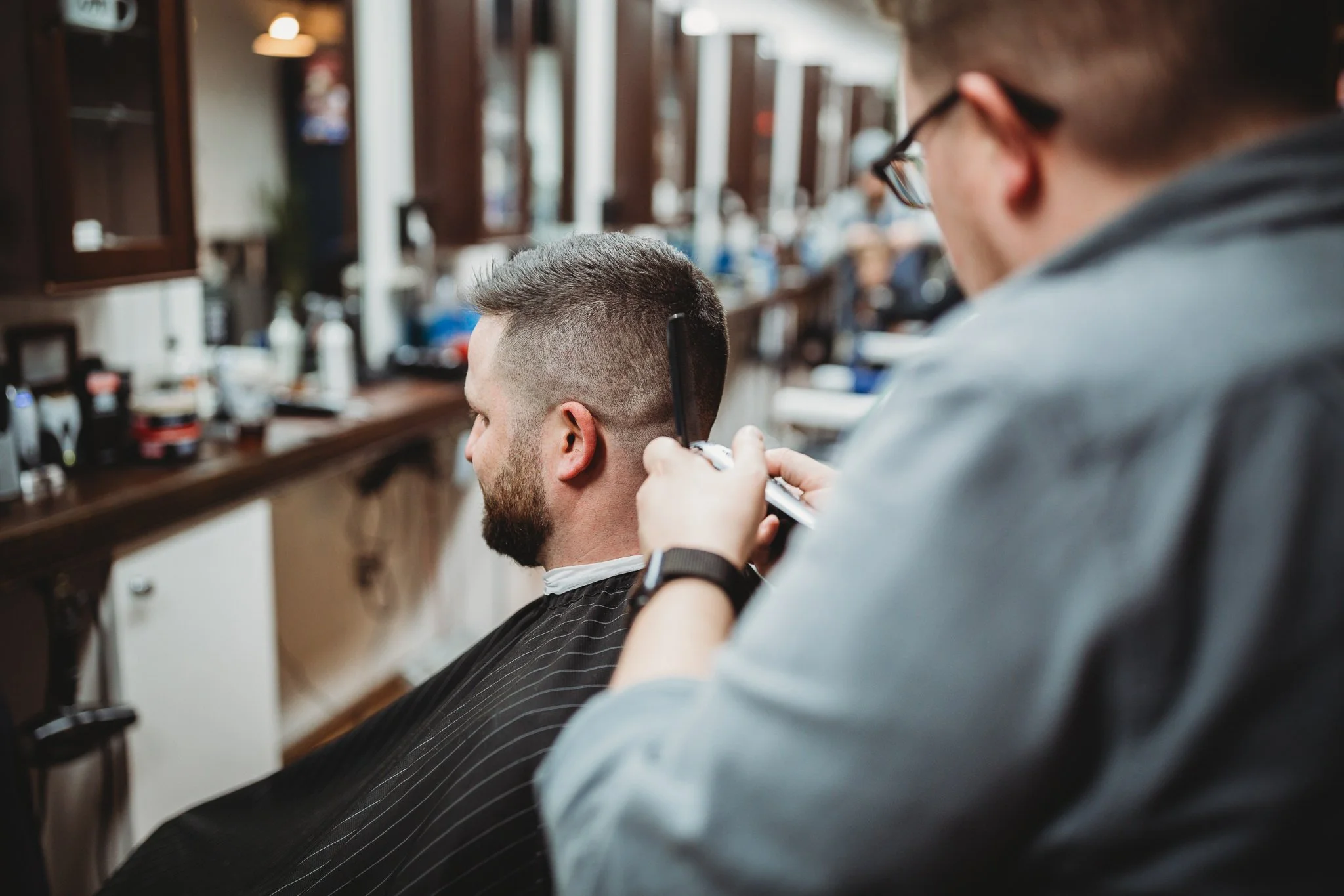 A man getting a haircut at a barbershop, with a barber trimming his hair using a pair of clippers.