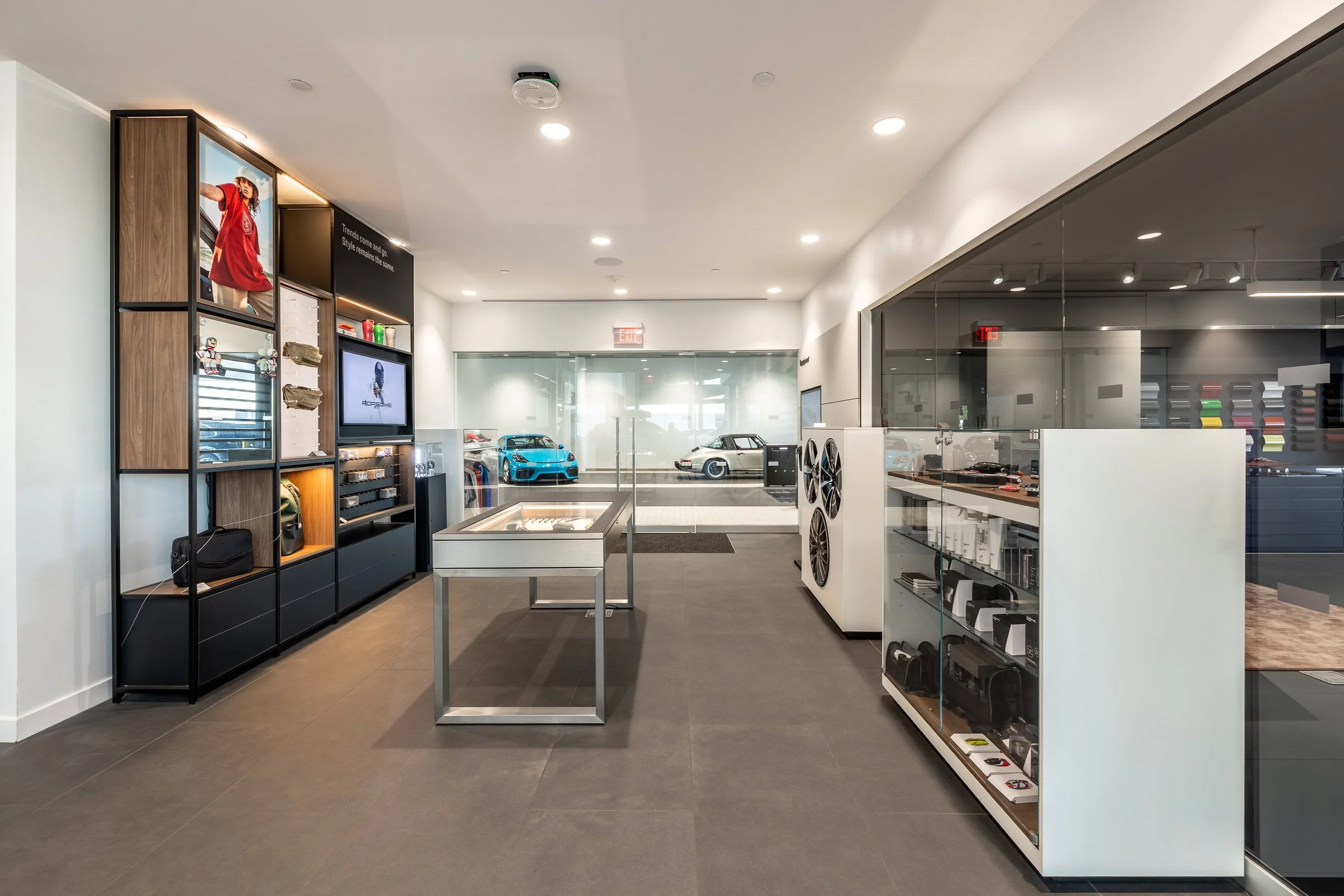Interior of a car dealership showroom with display cars, glass walls, shelves with merchandise, and informational displays.