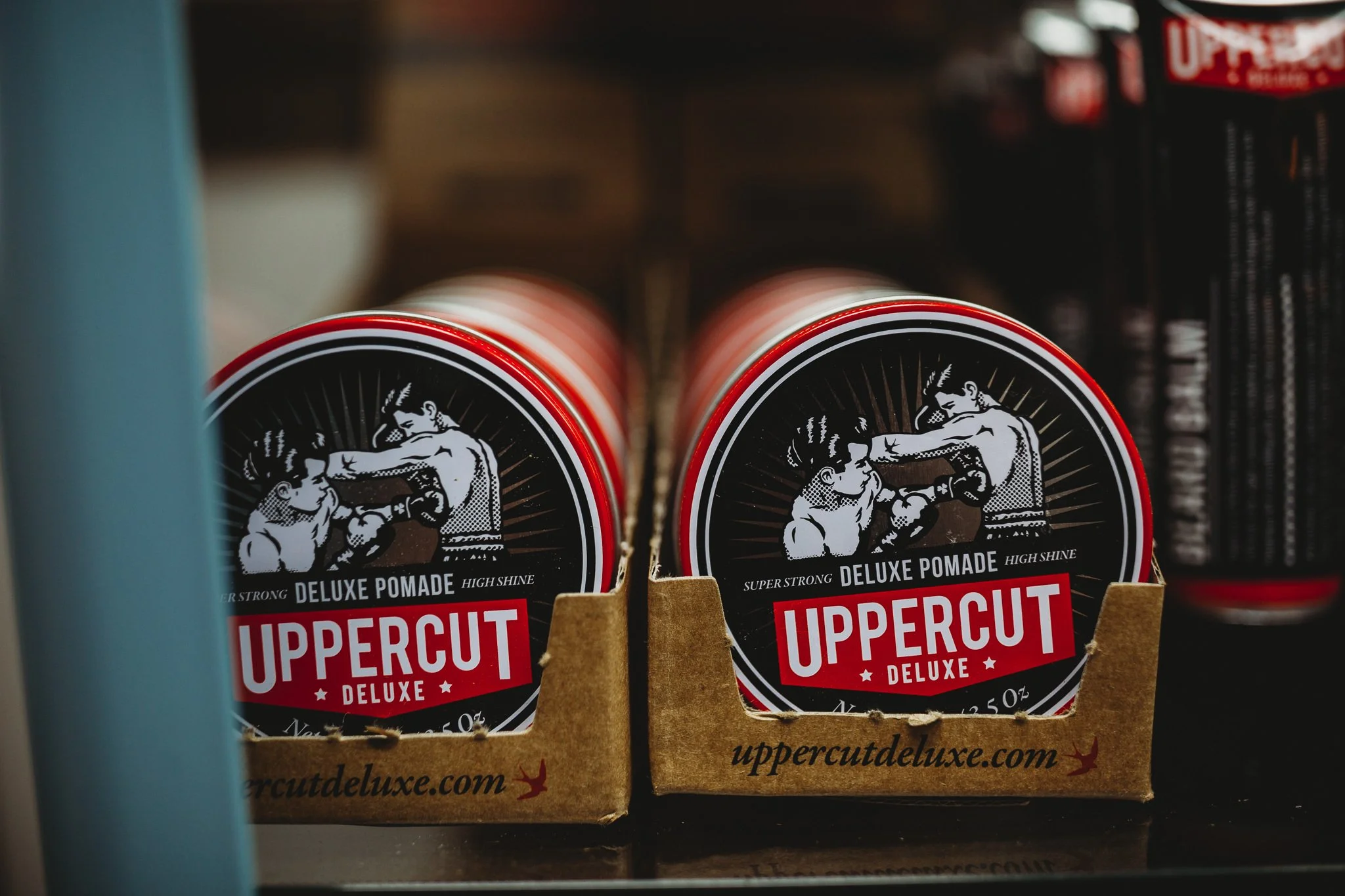 Two containers of Uppercut Deluxe Pomade on a store shelf.