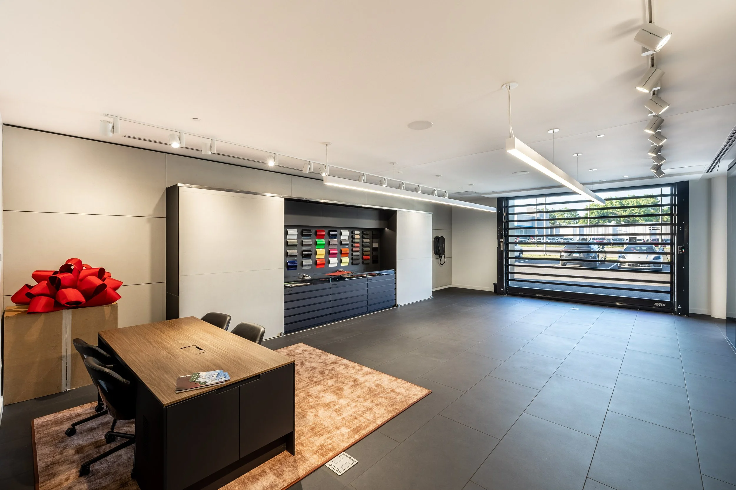 Empty modern garage or showroom with large garage door, front desk with chairs, and wall-mounted tools or supplies, illuminated with ceiling lights.