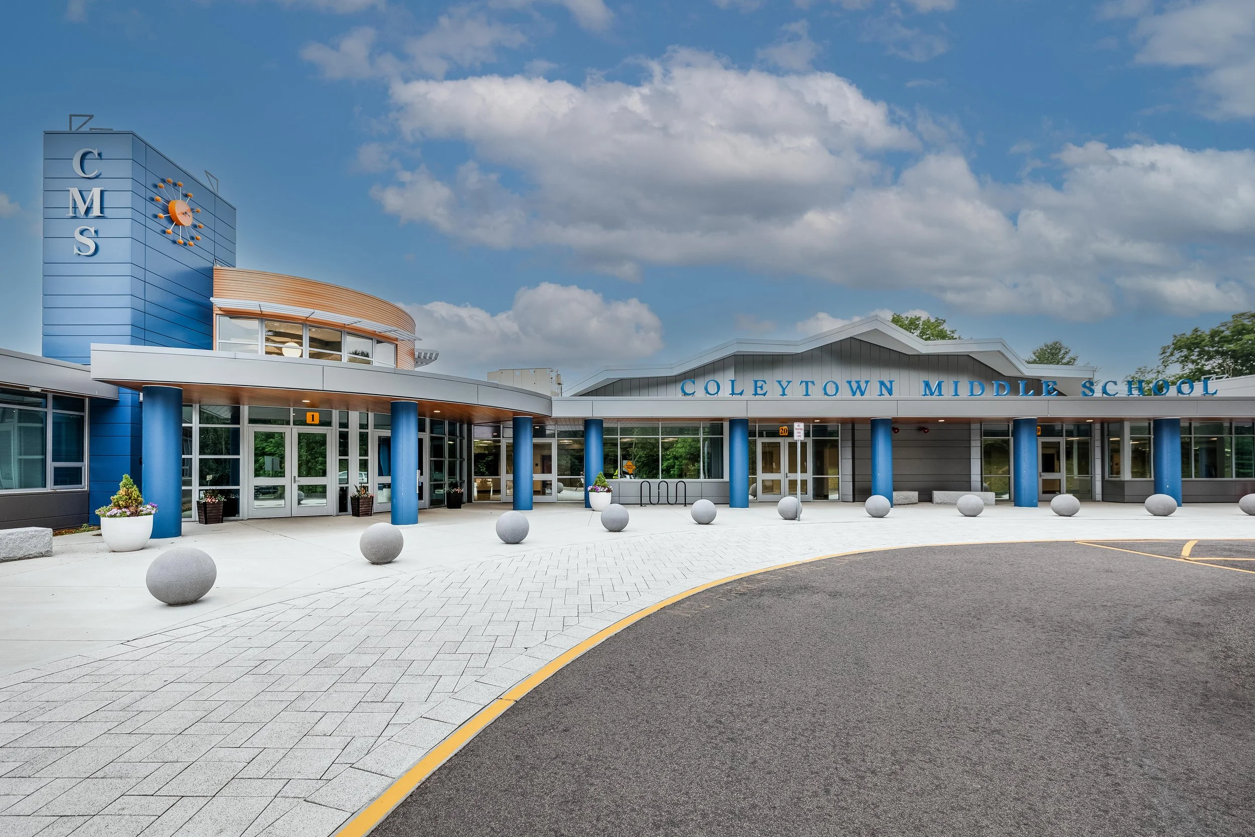 The exterior of Coleytown Middle School, a modern building with blue columns and large glass doors, under a partly cloudy sky.