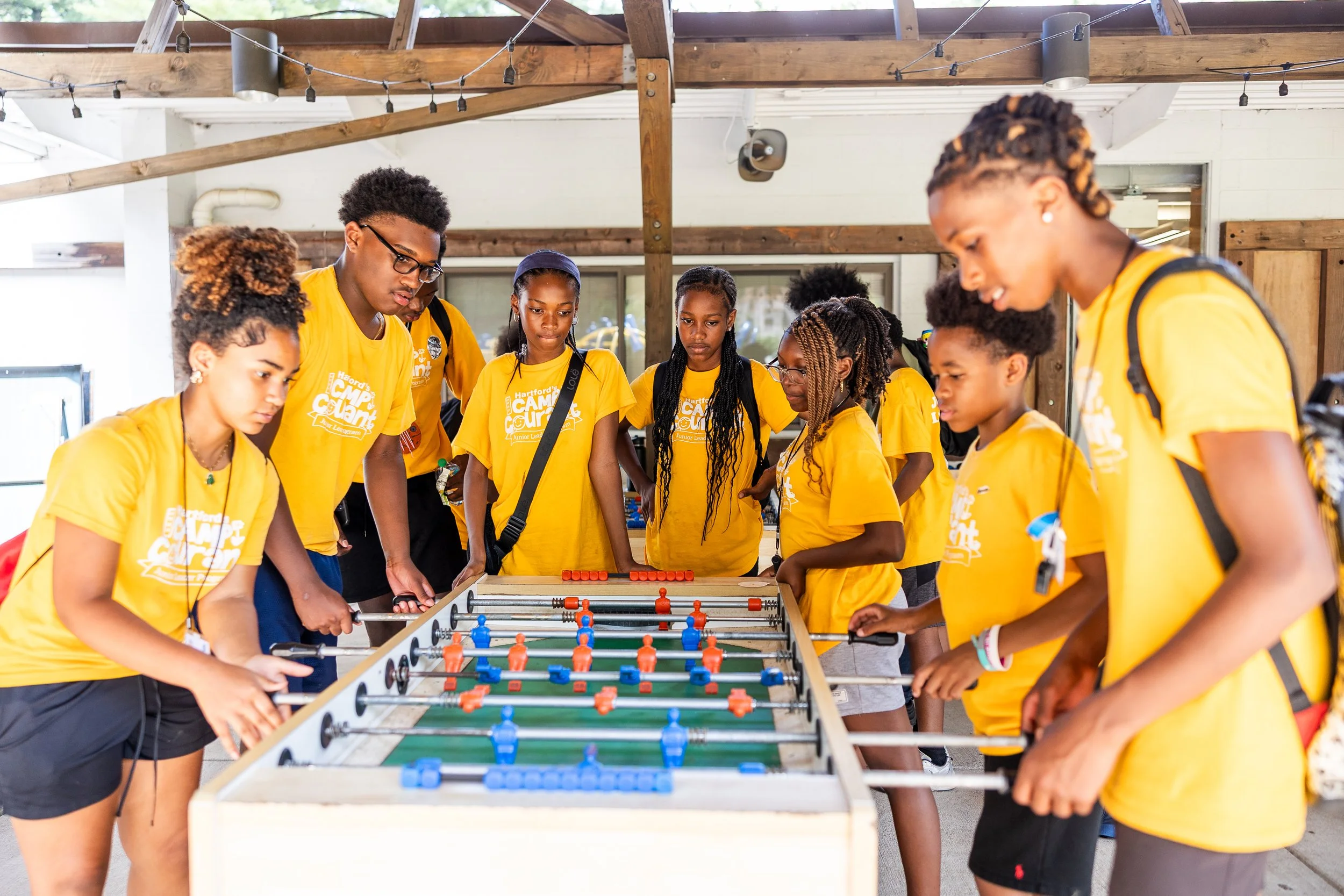 Group of children and teens in yellow T-shirts playing foosball at an indoor event.
