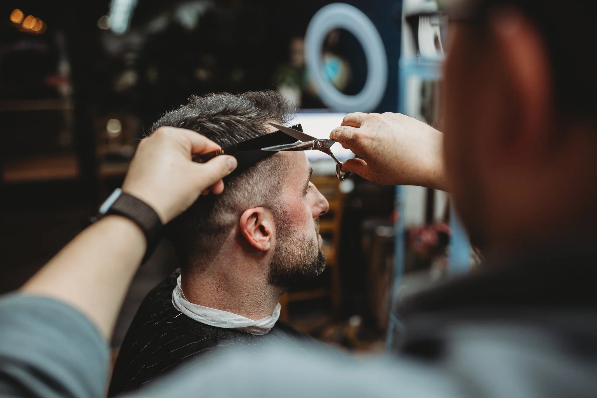 A man getting a haircut with scissors and clippers from a barber in a barbershop.