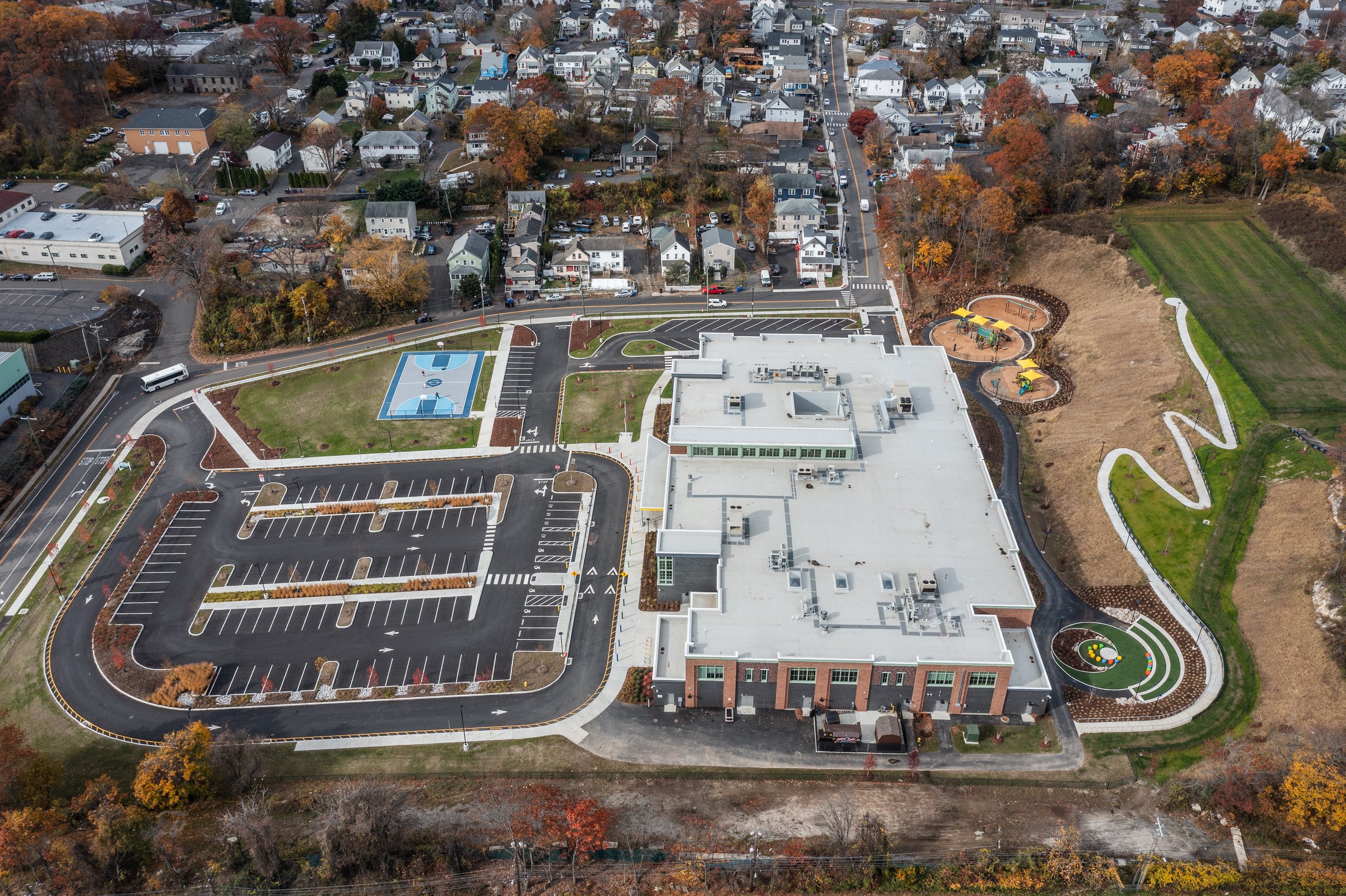 Aerial view of a school with a parking lot, playground, sports courts, and surrounding residential neighborhood.