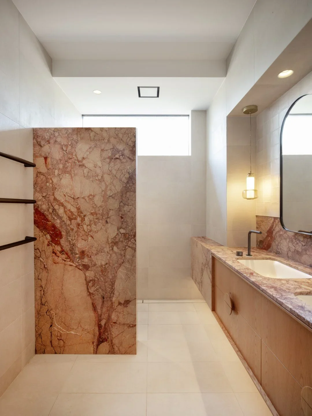 Modern bathroom with pink marble accents, a wall-mounted sink with marble countertop, mirror, small hanging light, and a partial marble privacy wall.