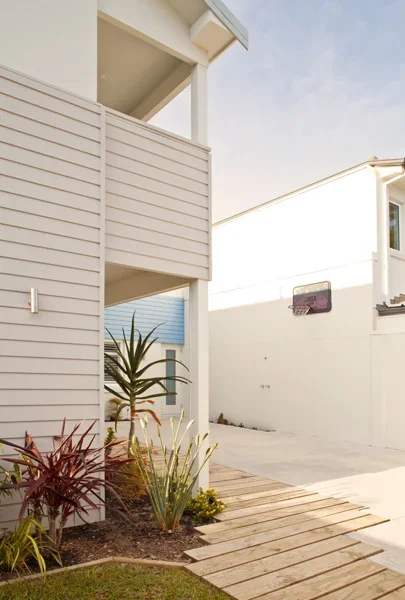 Exterior view of a modern house with siding, plants in the yard, wooden walkway, and a basketball hoop in the driveway.