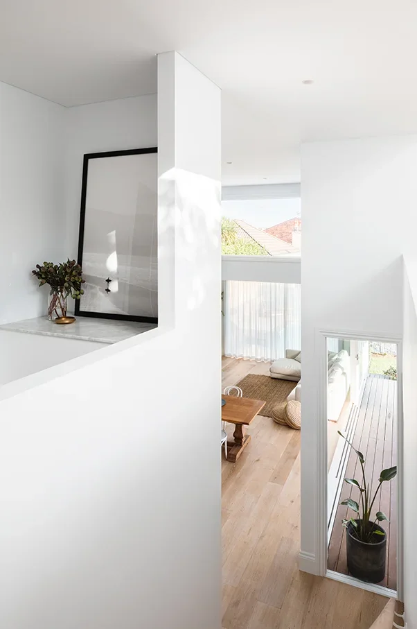 Modern living room with white walls, a small wooden table, a sofa, and large windows with curtains, seen from a partial upstairs view.