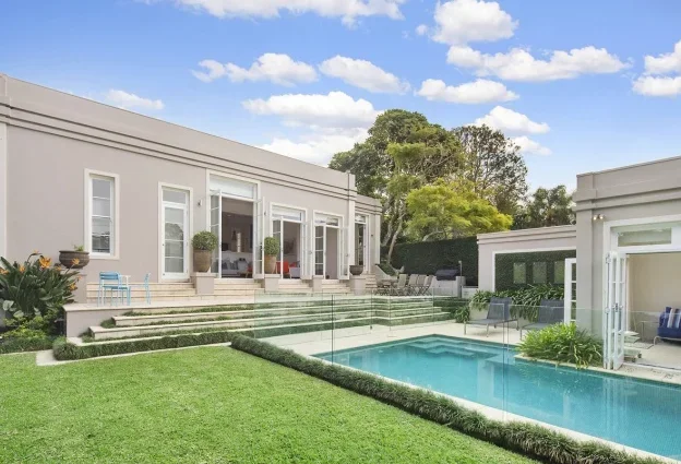 Modern house with a backyard swimming pool, green lawn, and outdoor seating area under a blue sky with clouds.