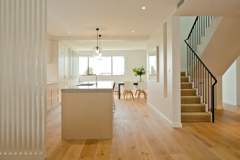 Open-plan kitchen and dining area with large window, white cabinetry, a kitchen island, and a staircase with beige carpet and black railing.