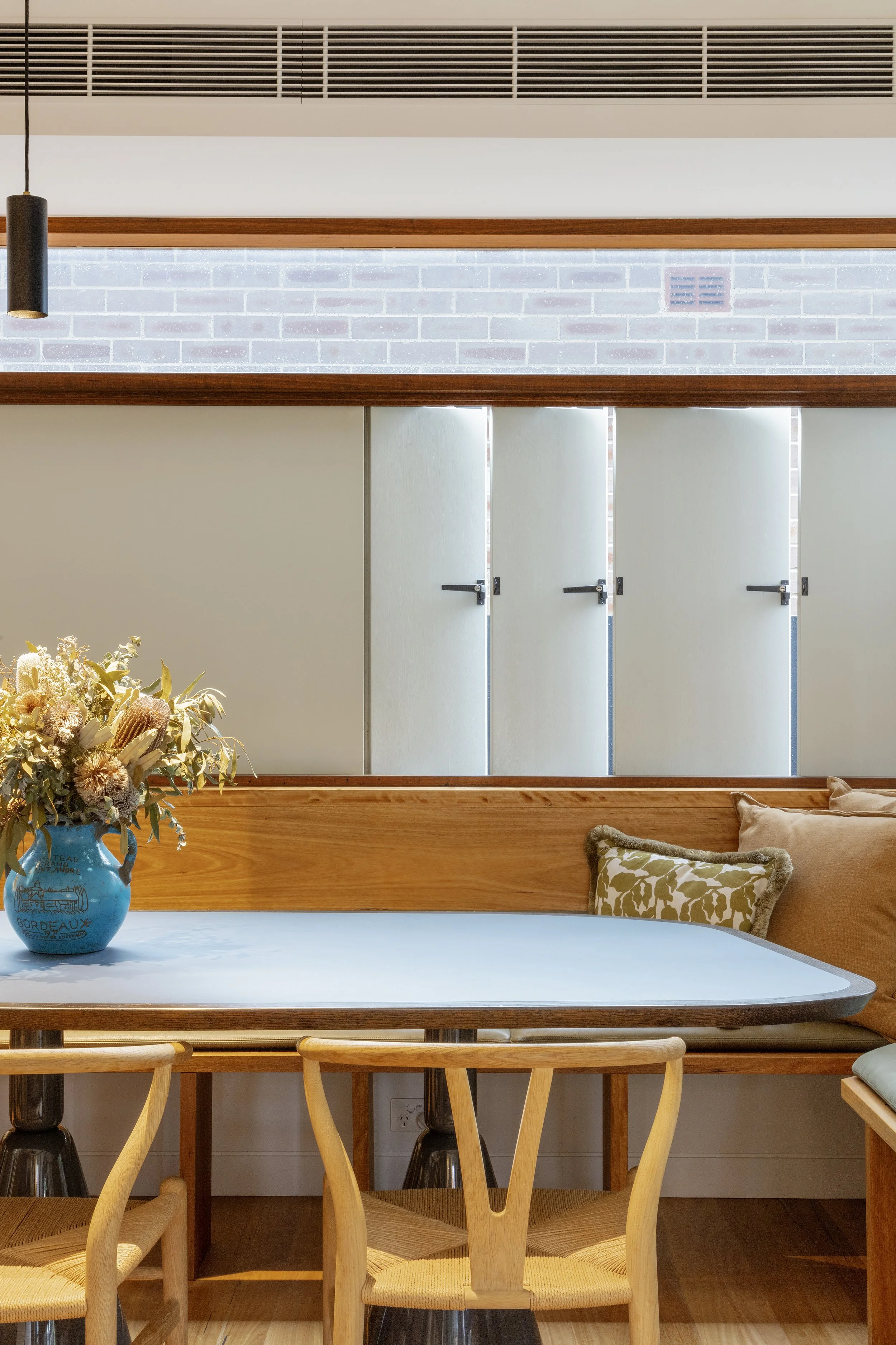 Dining area with a timber table, chairs and a blue vase of flowers.