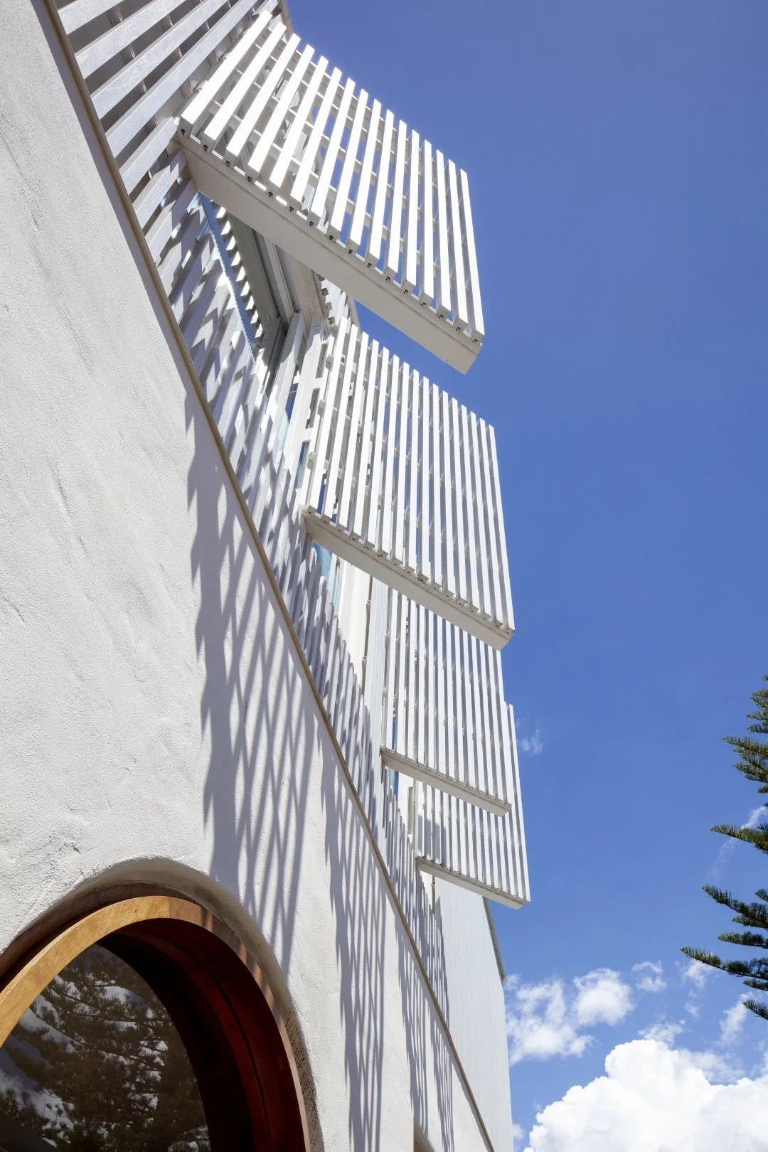 Close-up of a white building with modern, white, slatted balcony railings against a bright blue sky with scattered clouds.