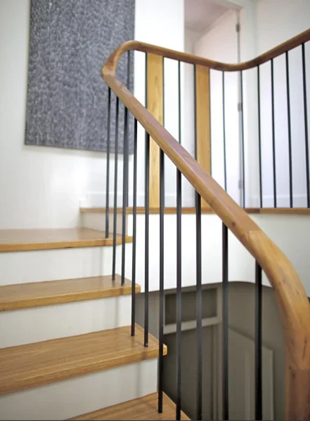Interior staircase with wooden handrail and black metal balusters, leading up to a white wall and a closed door.