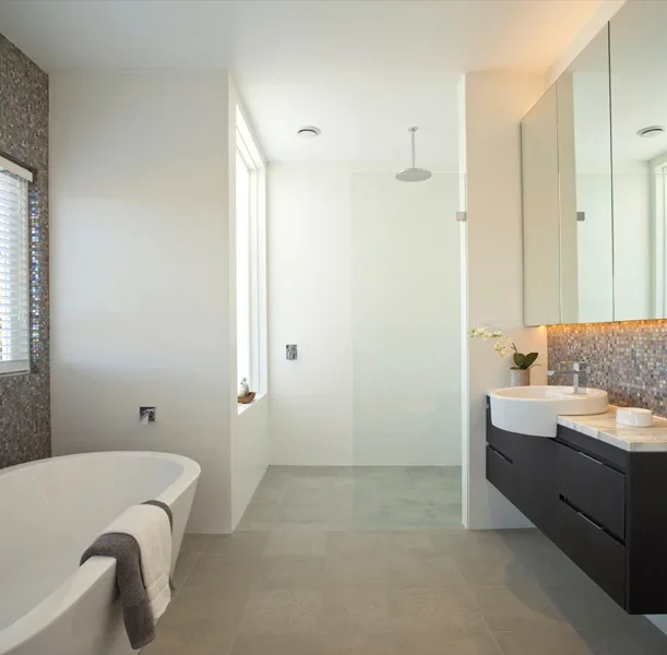 Modern bathroom with a free-standing bathtub, a walk-in shower, and a vanity with a white vessel sink, mirror cabinets, and a mosaic tile backsplash.
