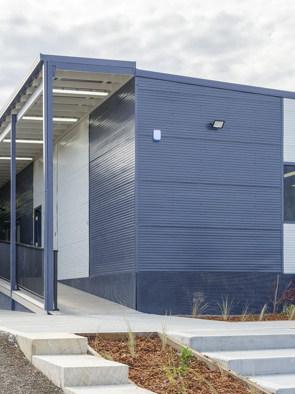 Modern building with navy blue and white siding, a ramp, and concrete stairs outside.