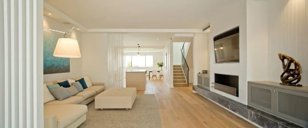Modern living room with beige sectional sofa, coffee table, wall-mounted TV, fireplace, and wooden flooring.