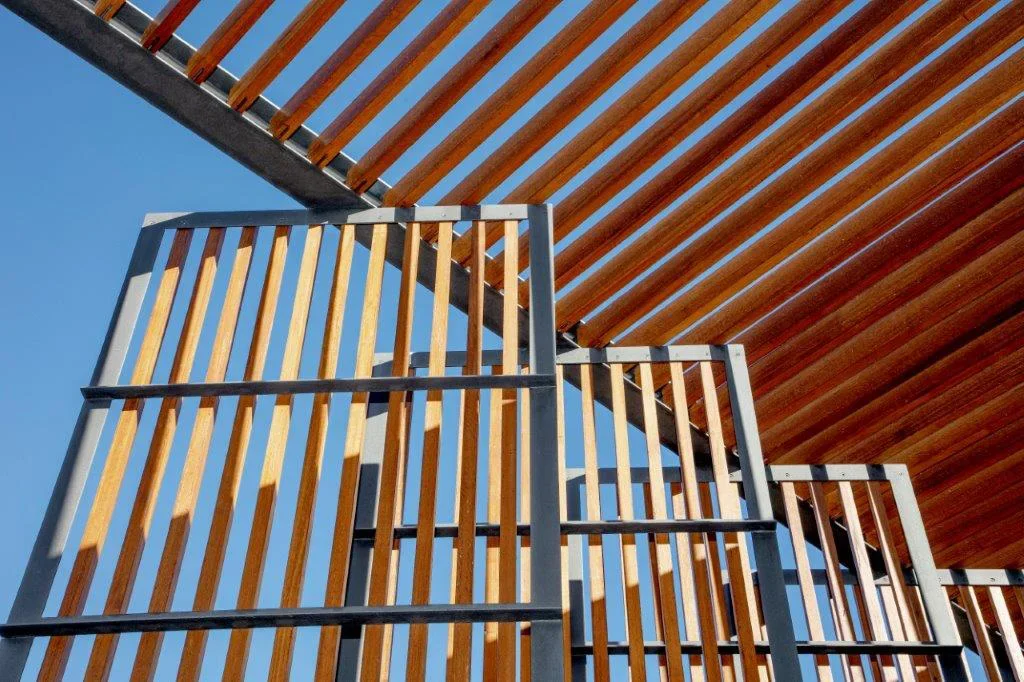 A modern architectural structure with wooden slats and metal framing against a blue sky.