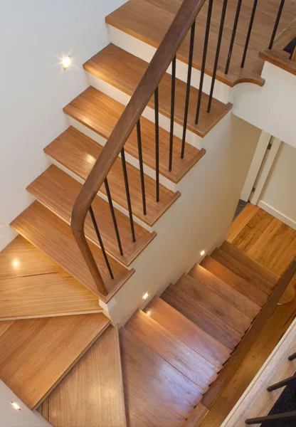 Wooden staircase with black metal spindles and handrail, viewed from above, leading down to a lower floor.