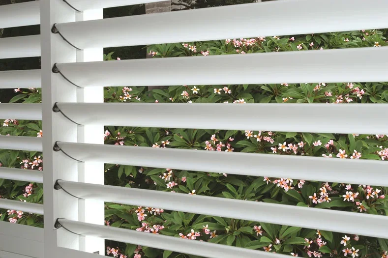 White louvered window with pink and white flowers and green leaves visible outside.