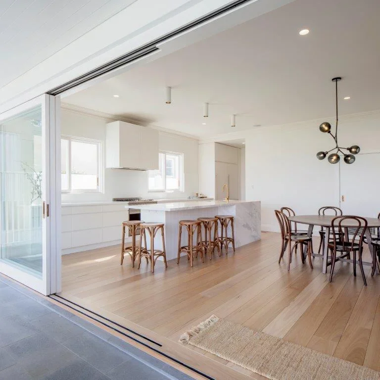 Modern kitchen and dining area with white cabinets, wooden barstools, a dining table with wooden chairs, and a contemporary chandelier.