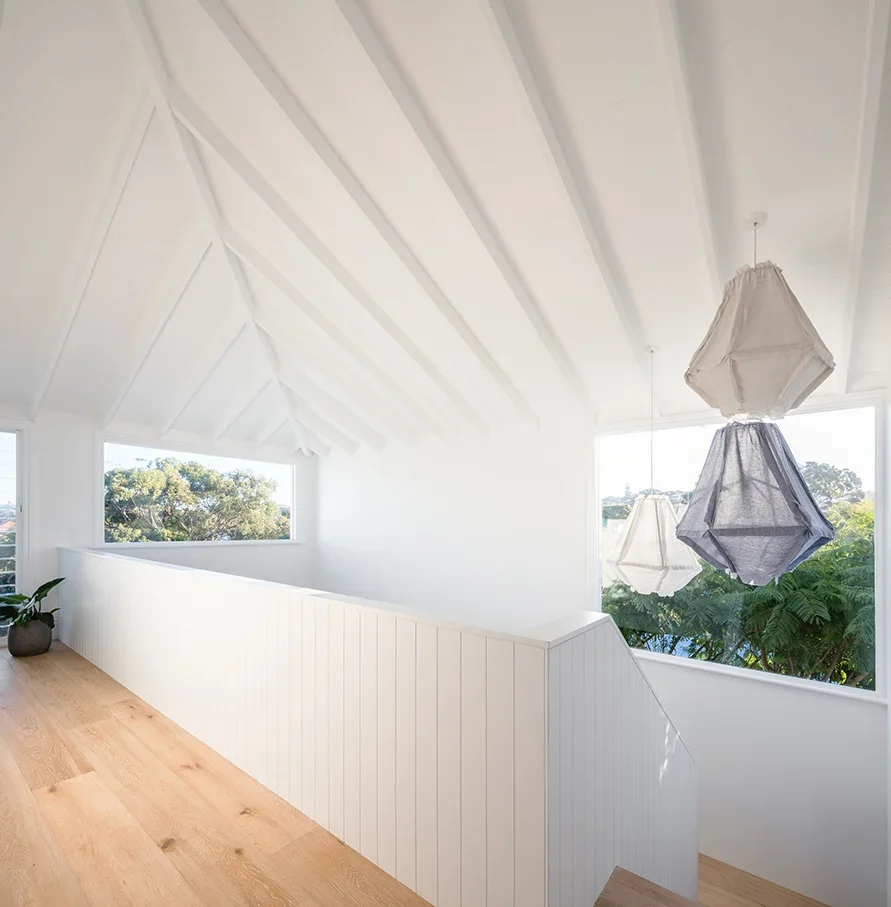 Bright, modern stairway landing with white walls, wooden floor, two hanging pendant lights with gray and white shades, and large windows with view of trees outside.
