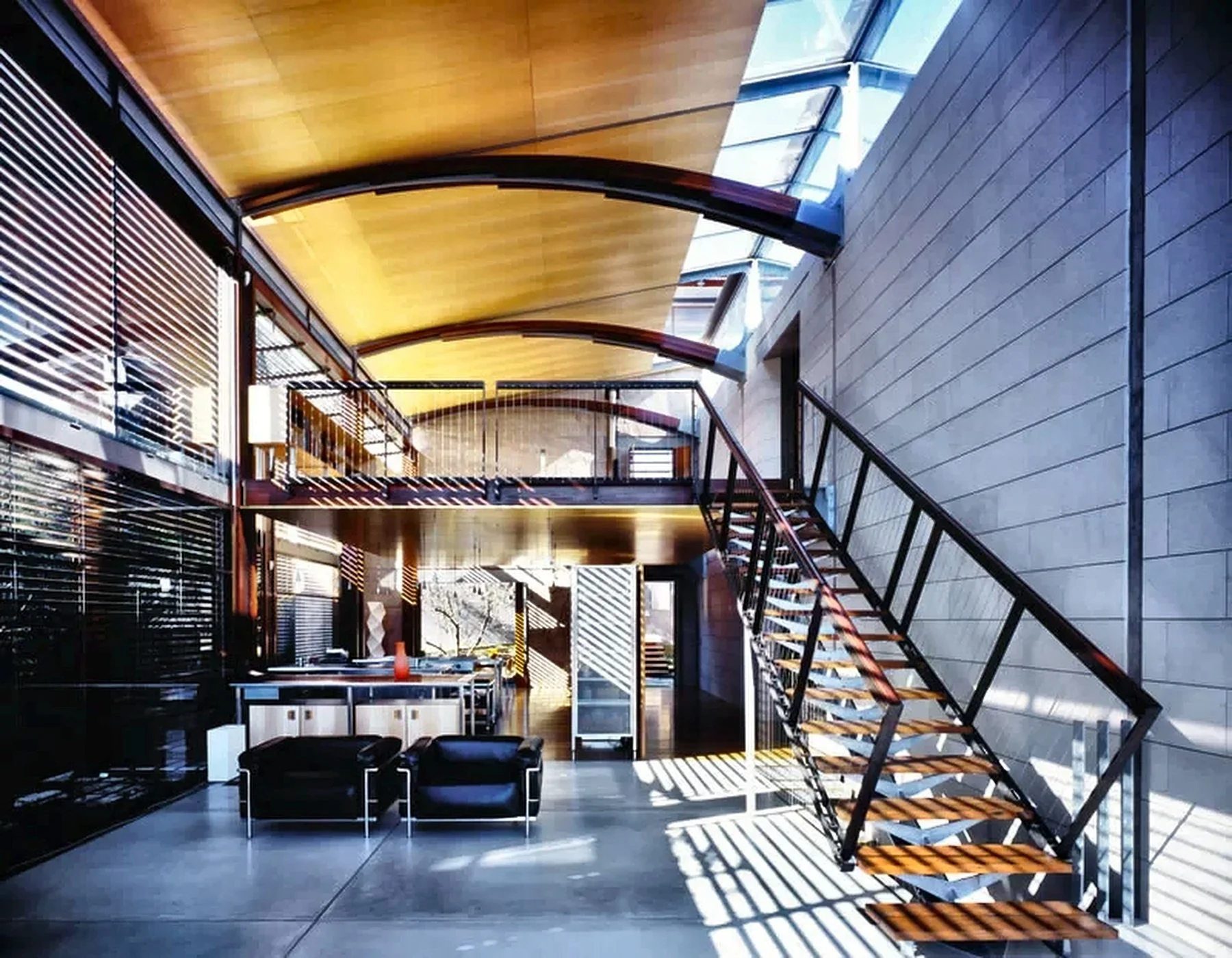 Designed by Peter Stutchbury. Modern interior with a staircase leading to a mezzanine, large windows on the ceiling, and sunlight casting shadows through blinds.