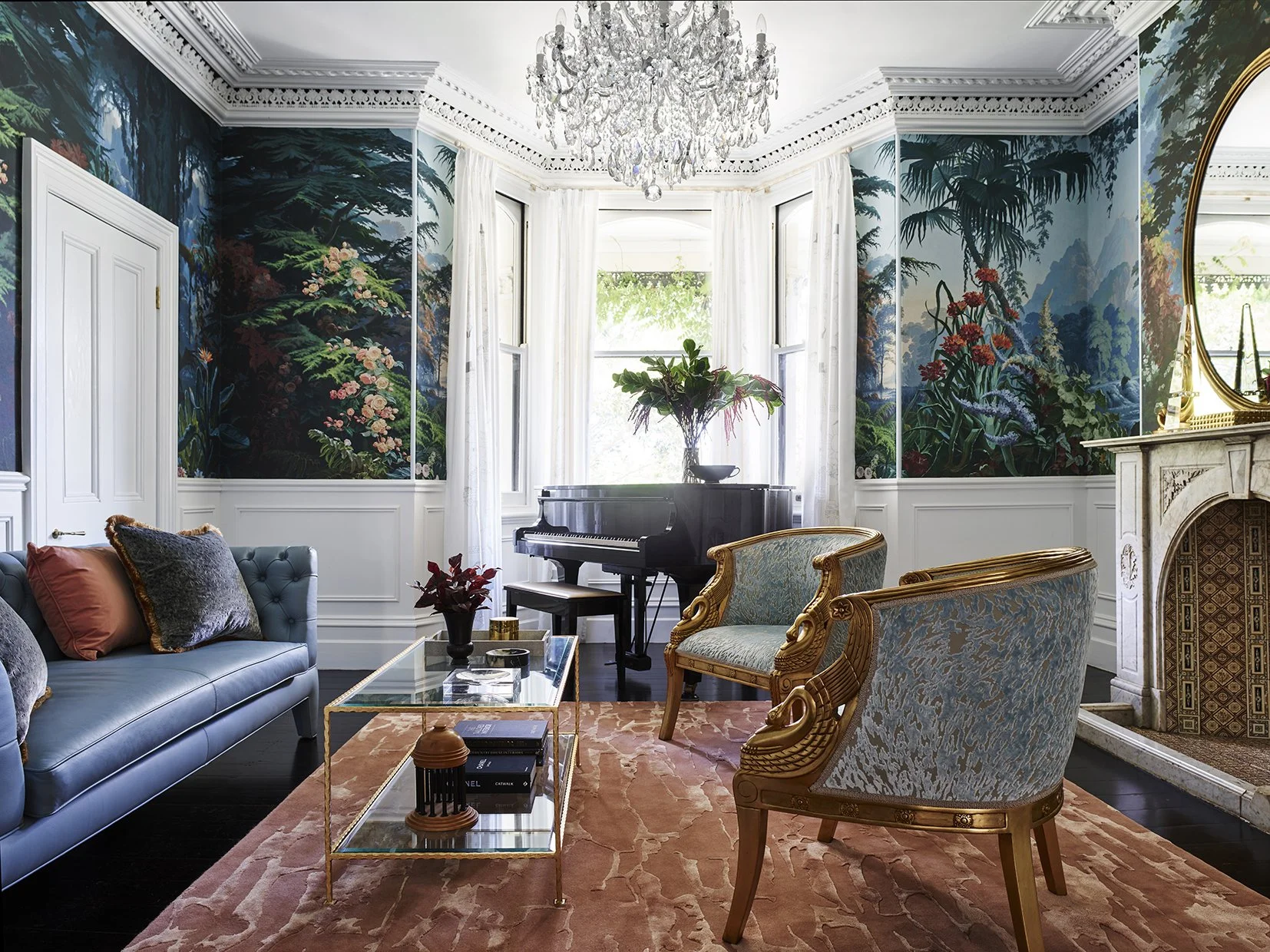  Light-filled heritage living room in a Newtown house featuring a grand piano, crystal chandelier, botanical mural wallpaper, marble fireplace and blue velvet seating.