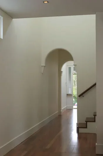 Interior hallway with wooden flooring, white walls, an arched doorway, and a staircase with a wooden handrail leading upstairs.