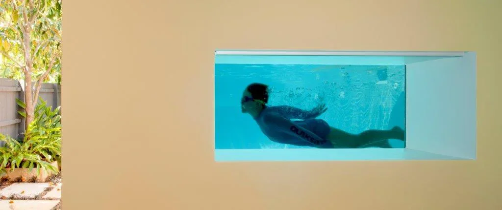 Child swimming underwater in a rectangular pool with a view of outdoor garden