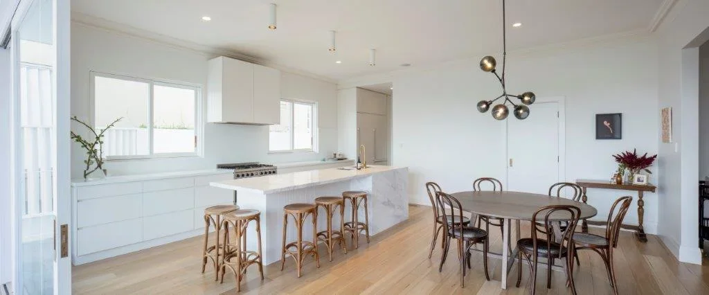 Modern kitchen and dining area with white cabinetry, a marble island, wooden bar stools, a round dining table with wooden chairs, minimal decor, and a pendant light fixture.