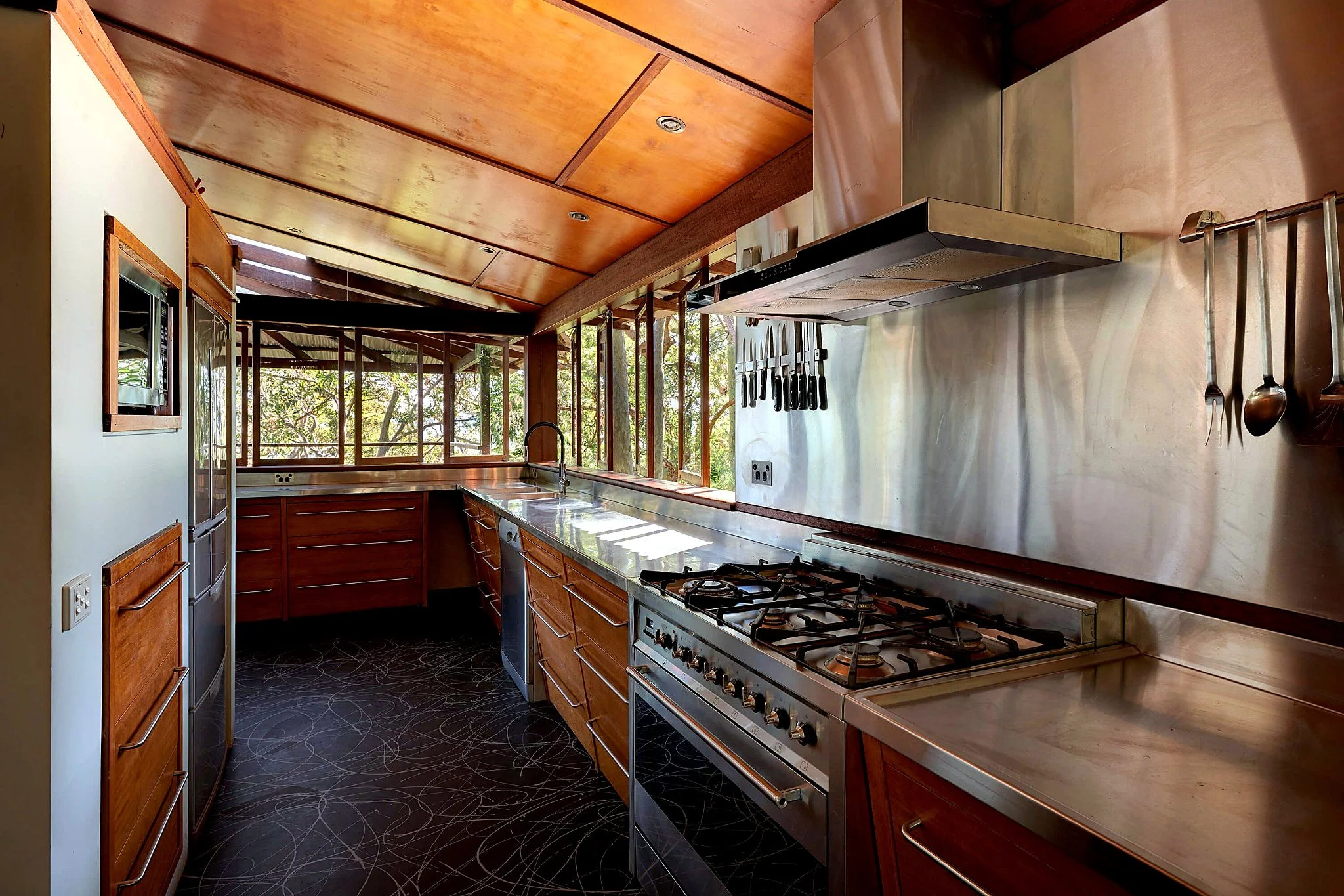 Timber and stainless-steel kitchen at Tree Top House, with windows overlooking the surrounding Avalon bushland.