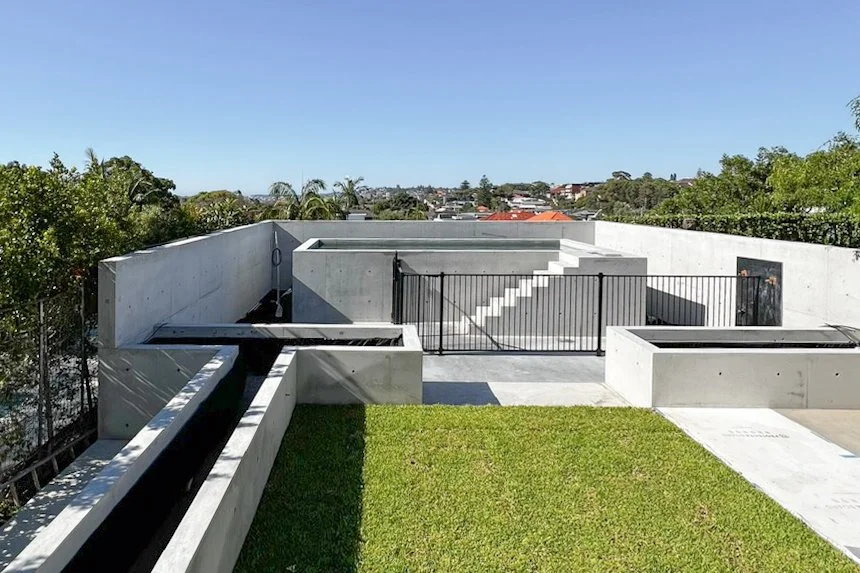 Modern rooftop with concrete walls, black metal gate, green grass, and clear blue sky.