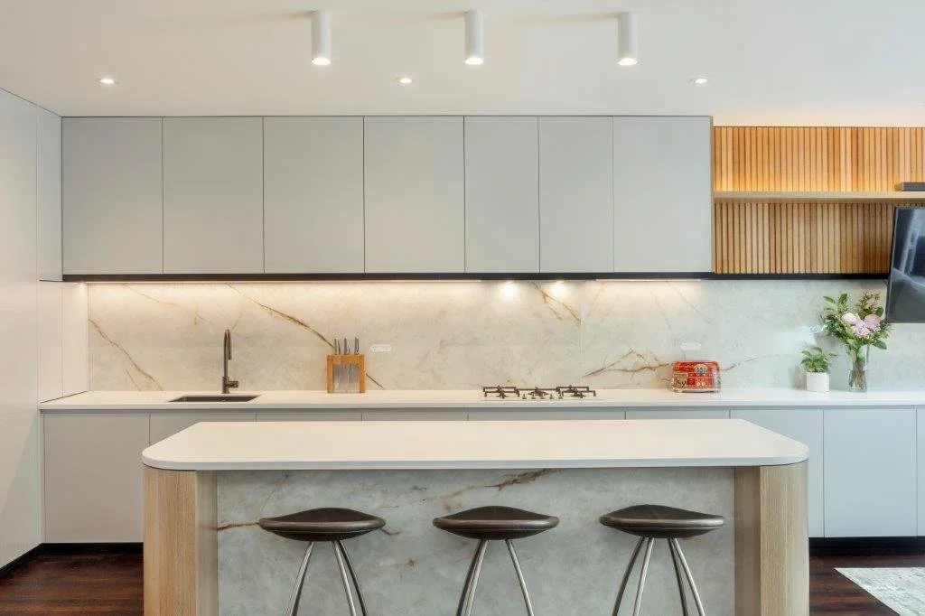 Modern kitchen with white cabinets, marble backsplash, and a white island with three bar stools.