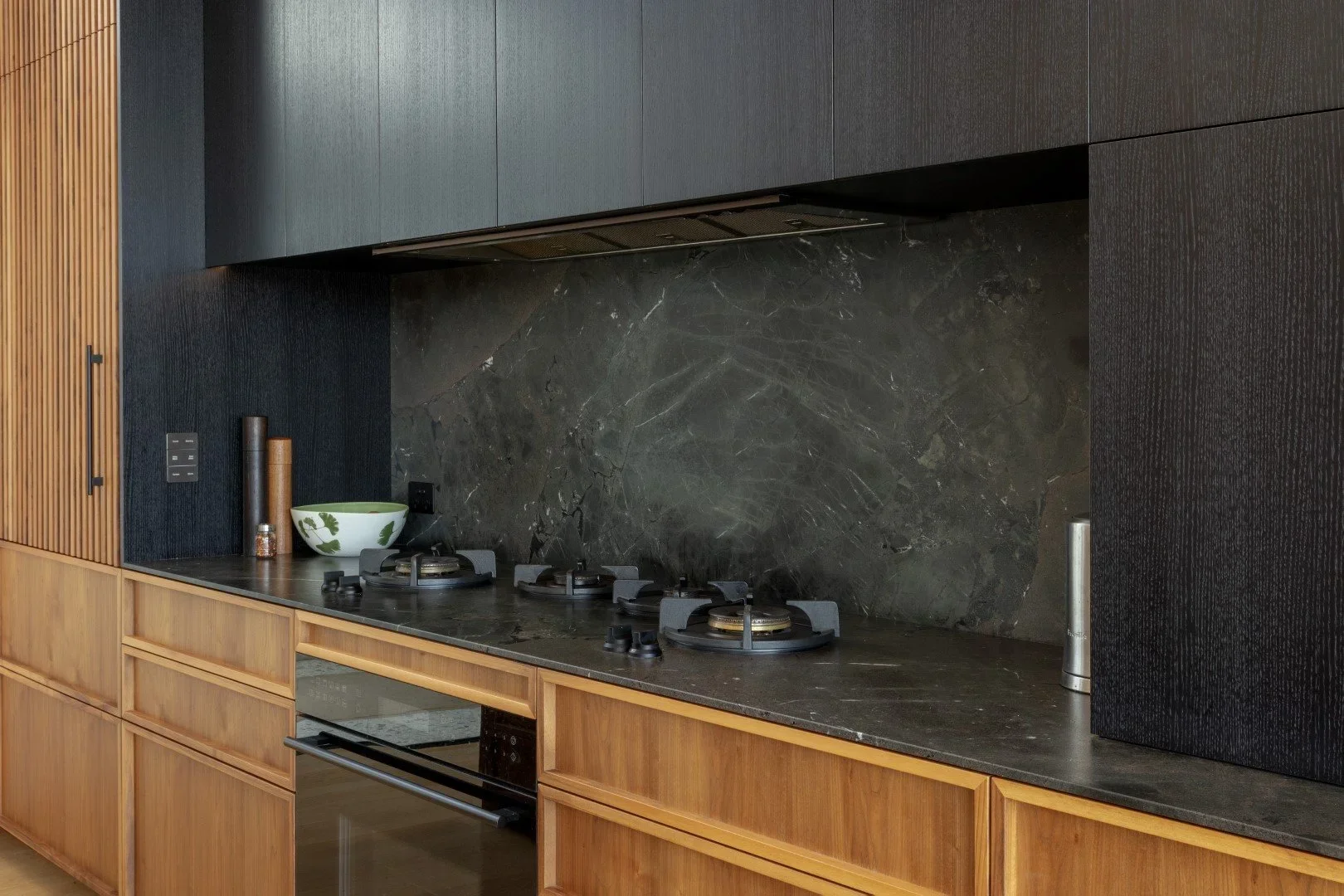 Modern kitchen with black and dark wood cabinetry, marble backsplash, and a built-in oven.