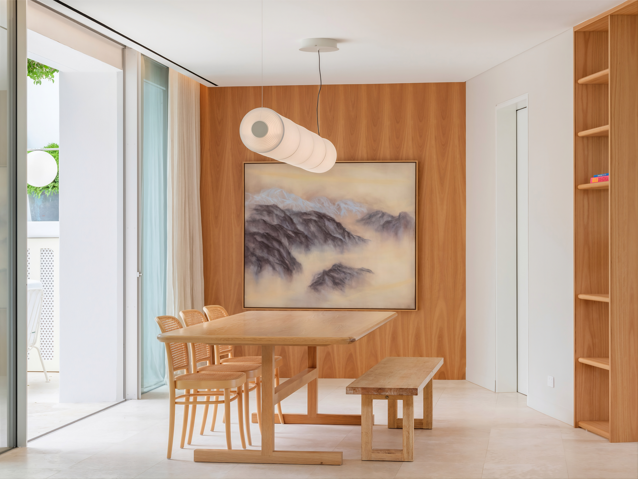 A warm and minimalist dining area in the Clovelly House project by To The Mil, defined by custom timber wall panelling, a handcrafted oak dining table and sculptural pendant lighting. Large sliding doors connect the space to the outdoor terrace, enha