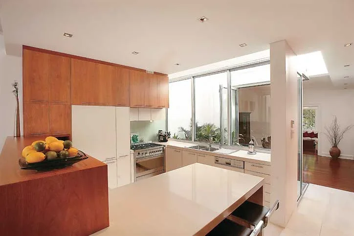 Modern kitchen with wooden cabinets, white countertops, large windows, and minimal decor.