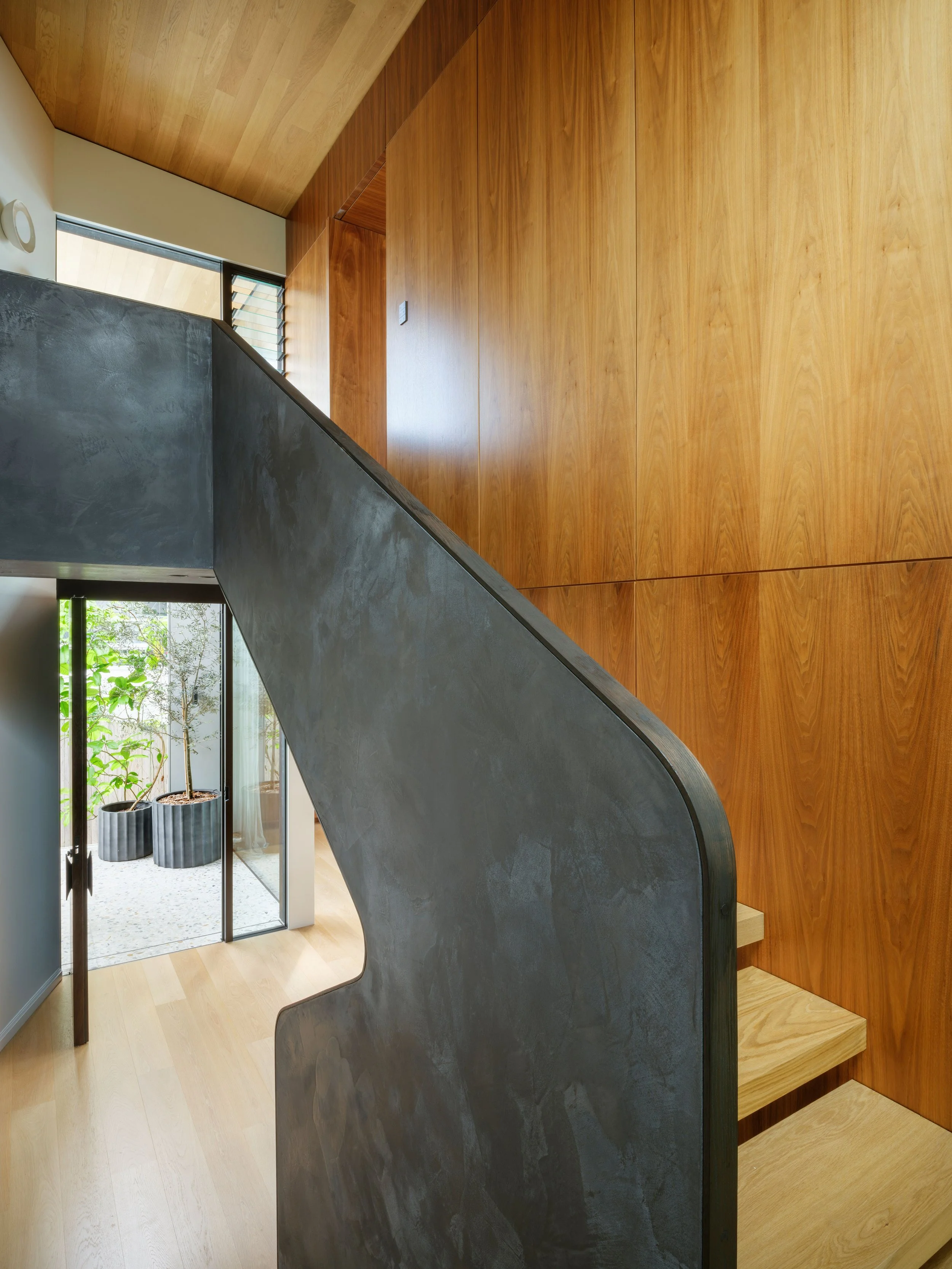 Curved balustrade and timber stairs set against warm timber panelling at the Blandford Street home.