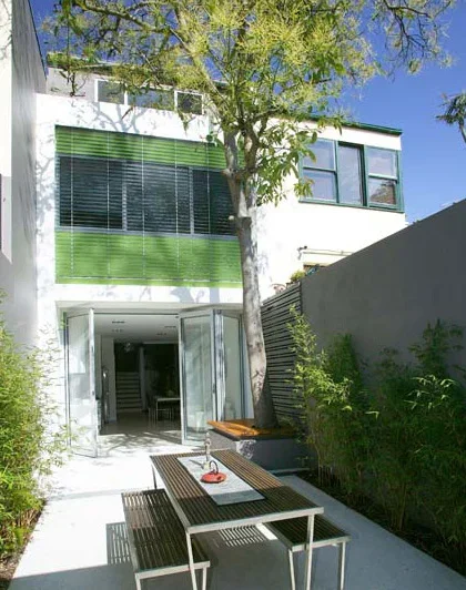 Modern house with a courtyard, featuring a tree, outdoor table with chairs, and large windows.